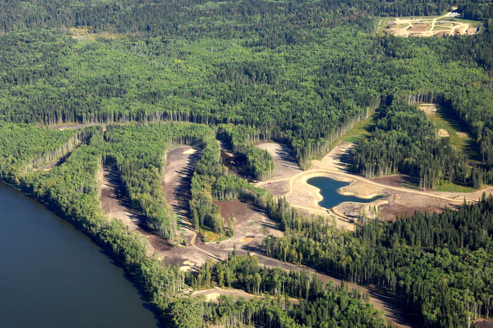 Aerial of a course cut through boreal forest beside a river